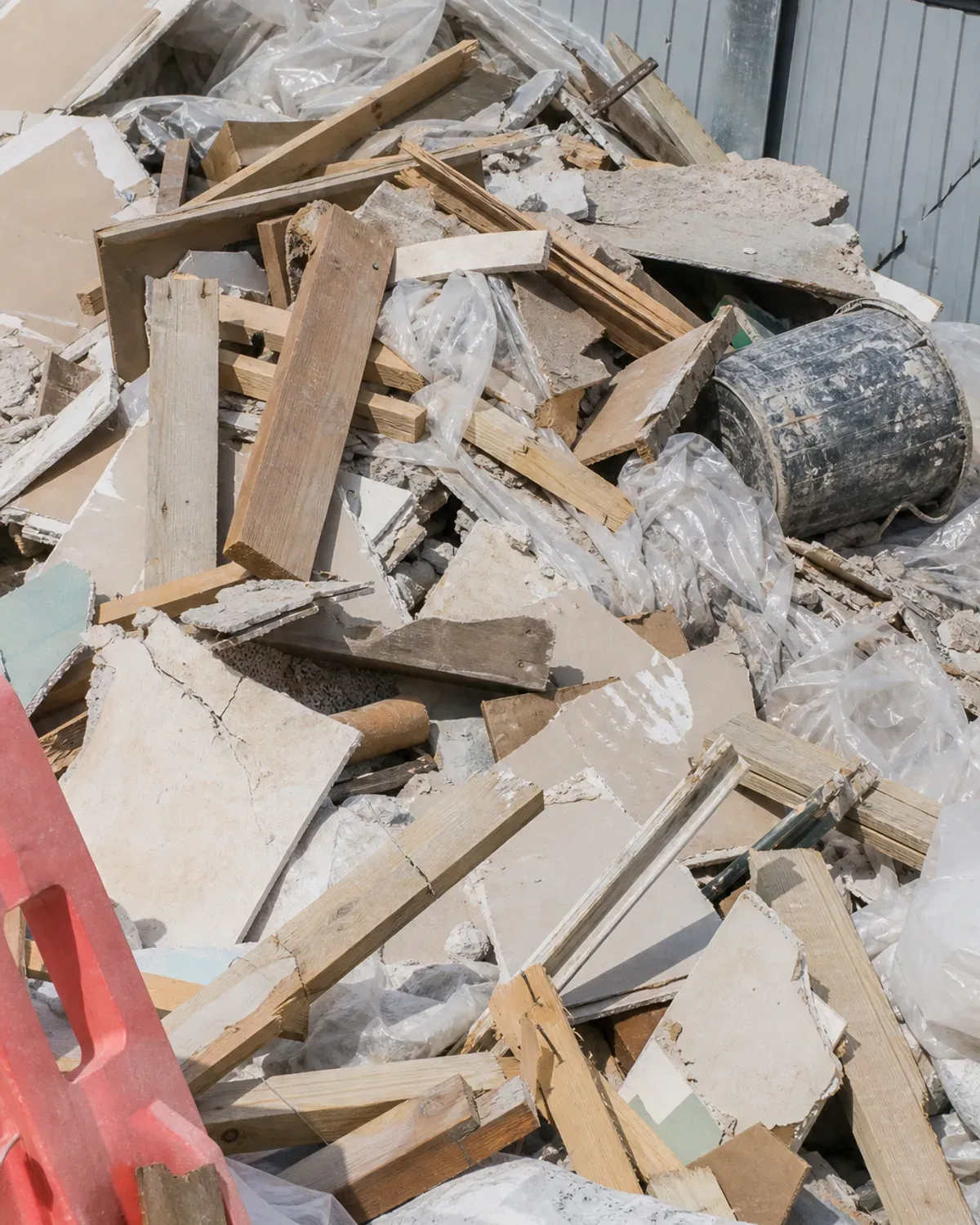 Unsorted heap of plasterboard, timber offcuts, plastic sheeting and rubble dumped against site hoarding